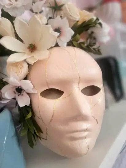 Close up of a cream coloured mask with gold kintsugi markings and a flower crown.