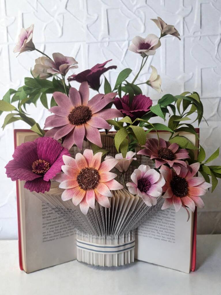 A book turned into a vase with maroon and pink flowers.