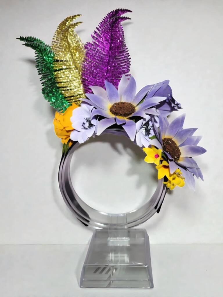 A mardi gras headband with green, gold and purple feathers and blue sunflowers and yellow stephanotis.