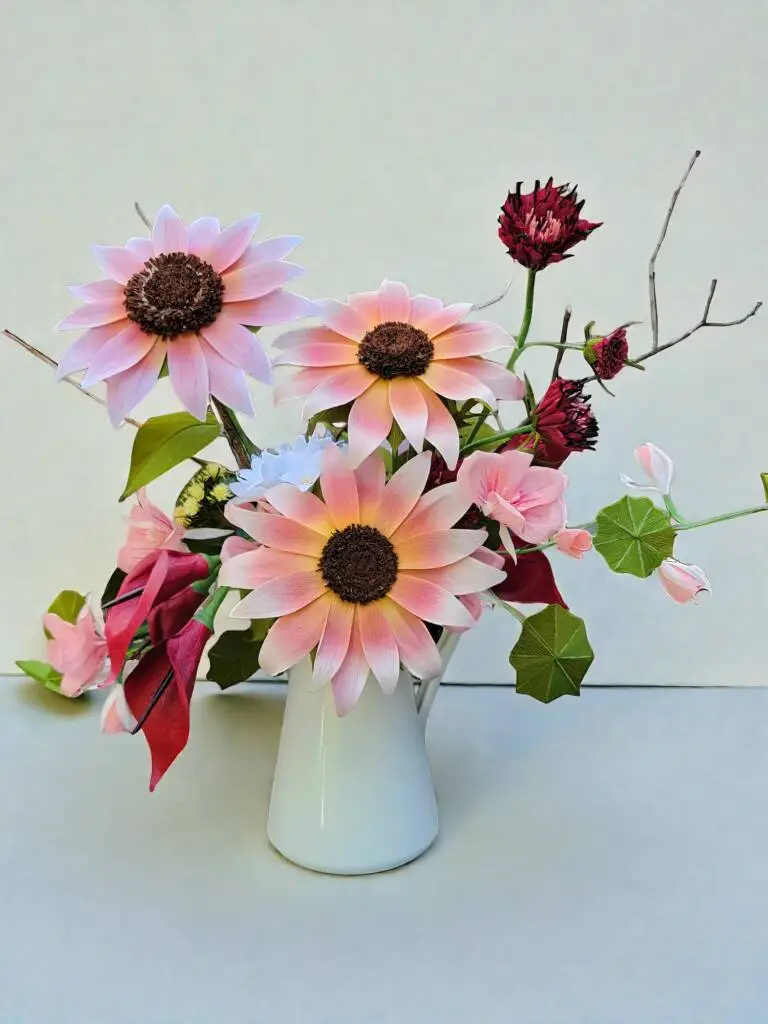 A bouquet of sunflowers, calla lilly in a white pitcher.